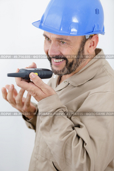 builder talking into walkie-talkie held flat in front of him. Стоковое фото, агентство Ingram Publishing / Фотобанк Лори