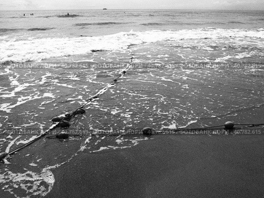 Buoys on a rope near sea water. The lifebuoys restraints to alert people to the depth of the water. Delimiting a place on a sandy beach between hotels. Wave with bubbles. Black white photo monochrome. Стоковое фото, фотограф Юлия Петровская / Фотобанк Лори
