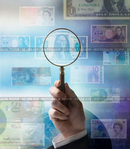 Businessman holding magnifying glass up to world currencies. 24316771. Стоковое фото, агентство Ingram Publishing / Фотобанк Лори