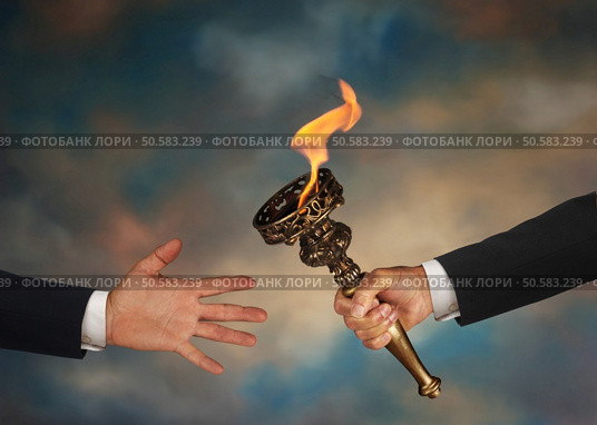 Businessman’s outstretched arm passing a flaming torch to another businessman’s open hand. Стоковое фото, агентство Ingram Publishing / Фотобанк Лори