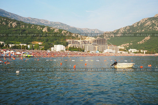 Canj, Montenegro 07.20.2024 Boats and a shore with vacationers, sunbathers and swimmers. Hotels, sun umbrellas, Adriatic waves, buoys. Beach tourism. Vacation travel. Summer day. Pebble rock beach. Редакционное фото, фотограф Юлия Петровская / Фотобанк Лори