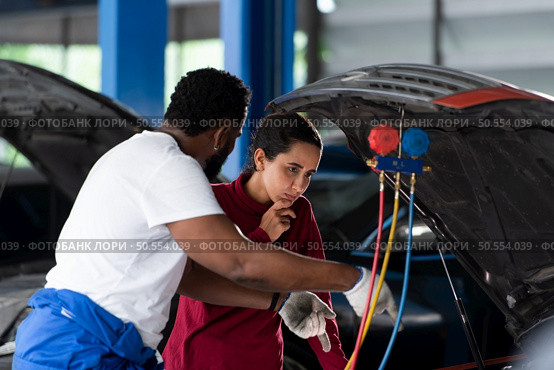Car mechanic working in an auto repair shop explain to customer after inspecting the operation of the car’s air conditioner and refrigerant. Стоковое фото, агентство Ingram Publishing / Фотобанк Лори