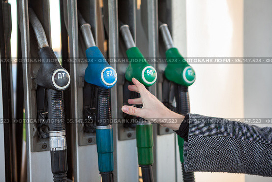 Caucasian female hand stretching to fuel nozzle with regular unleaded petrol, close up view. Стоковое фото, фотограф Кекяляйнен Андрей / Фотобанк Лори
