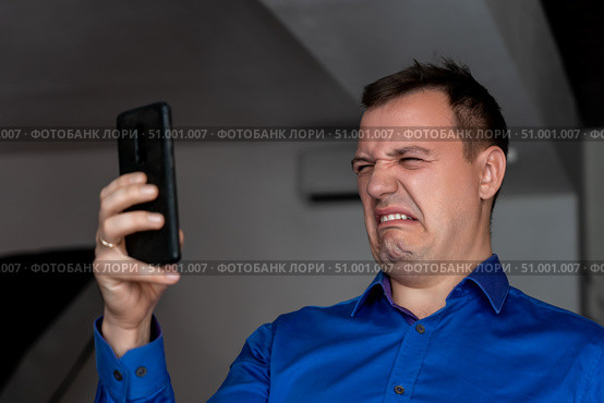 Caucasian man crying while looking at text message in cellphone. heartbroken millennial man looks at screen of smartphone and grieves. Tragedy in the family. Concept of Feeling Stressed, Anxiety. Стоковое фото, фотограф Данила Большаков / Фотобанк Лори