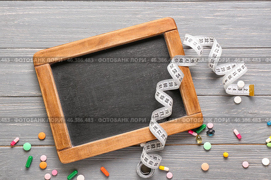 Chalkboard with measuring tape and pills on wooden background. Concept of anorexia. Стоковое фото, фотограф Pixel_shot / Фотобанк Лори