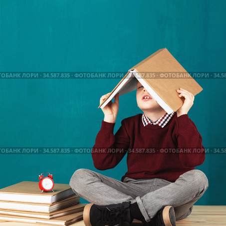 Cheerful smiling little school boy with big books on his head having fun against turquoise wall. Стоковое фото, фотограф Nataliia Zhekova / Фотобанк Лори