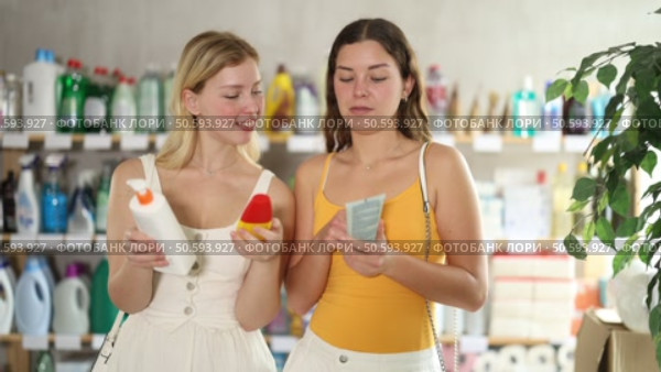 Cheerful young besties in light summer clothes examining bottles of sunscreen and tanning lotion in store, discussing choice of product ensuring skincare and UV protection while preparing for vacation. Стоковое видео, видеограф Яков Филимонов / Фотобанк Лори