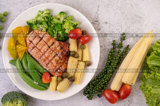 Chicken steak topped with white sesame, peas, tomatoes, broccoli and pumpkin in a white plate. Стоковое фото, агентство Ingram Publishing / Фотобанк Лори