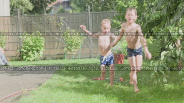 Children Joyfully Playing in Sprinkler Water During a Warm Summer Day Under the Sun. Стоковое видео, видеограф Olesia Kondrateva / Фотобанк Лори