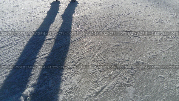 Children ride in a city park on an ice rink. Feet skater while skating on ice. The low winter sun weakly illuminates the ice. Dark shapes and long shadows on the surface. Sports movements. Стоковое фото, фотограф Юлия Петровская / Фотобанк Лори