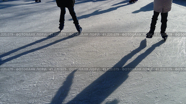 Children ride in a city park on an ice rink. Feet skater while skating on ice. The low winter sun weakly illuminates the ice. Dark shapes and long shadows on the surface. Sports movements. Стоковое фото, фотограф Юлия Петровская / Фотобанк Лори