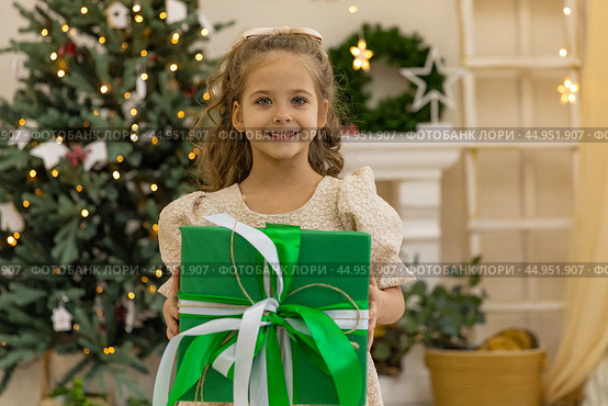Christmas holidays. Happy little smiling girl holding box near the Christmas tree. Happy girl unwrapping Christmas present. Holidays and celebrations concept. Стоковое фото, фотограф Ирина Михайличенко / Фотобанк Лори