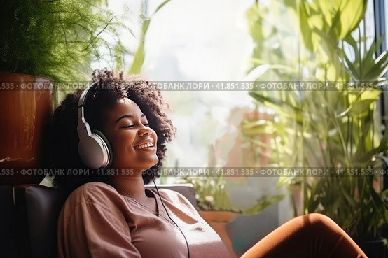 Chubby young dark skinned women sits in relaxed posture listening music with headphones among plants. Стоковое AI-изображение, AI-художник Наталья Семкина / Фотобанк Лори
