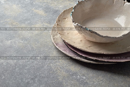 Clay handcraft empty plates, bowls, covered with glazed on a gray concrete surface with space for text. Flat lay. Traditional souvenir porcelain handmade colorful plate and bowl on a gray concrete background. Стоковое фото, агентство Ingram Publishing / Фотобанк Лори