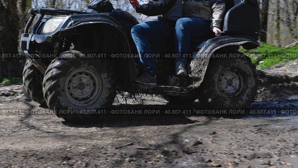 Close-up of a dirty black ATV riding on a dirt forest road. Water is flowing from it as it has just passed through a puddle. Side view. Extreme type of outdoor activities. Riding on a quad bike. Стоковое фото, фотограф Воловодов Владимир / Фотобанк Лори