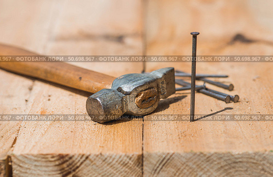 Close-up of a hammer and nails on wooden boards. Hand tools, old construction tools. Стоковое фото, фотограф Photojuli / Фотобанк Лори