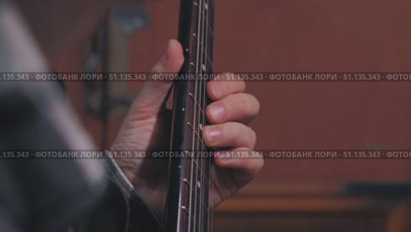 Close-up of a man's hand pressing strings to the fingerboard of an electric guitar. Warm muted background emphasizes attention to details. Work of a musician in a studio. Стоковое видео, видеограф Воловодов Владимир / Фотобанк Лори