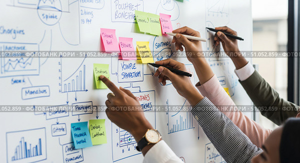 Close up of business team brainstorming on whiteboard, colleagues collaborating on project strategy using sticky notes and drawing charts in office meeting. Стоковое AI-изображение, AI-художник Павел Муравьев / Фотобанк Лори