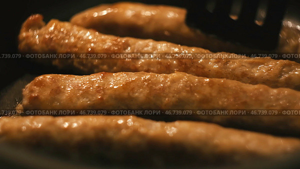Close-up of thin long pork sausages in natural casing fried on the pan. Стоковое фото, фотограф David Kashakhi / Фотобанк Лори