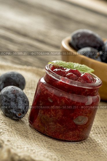Closeup of a glass jar full of home made freshly cooked plum jam with two ripe plums next to it placed on a linen cloth. Стоковое фото, агентство Ingram Publishing / Фотобанк Лори