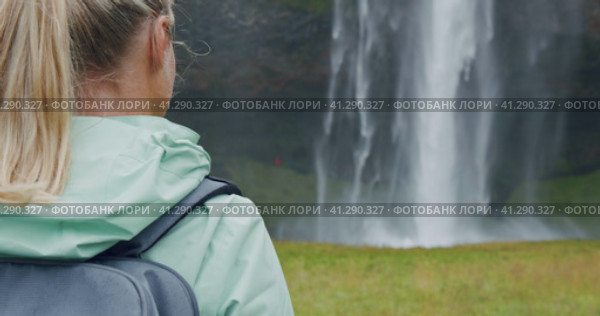Closeup of female traveler back with backpack loking to Beautiful Seljalandsfoss waterfall Iceland. Стоковое видео, видеограф Igor Tichonow / Фотобанк Лори