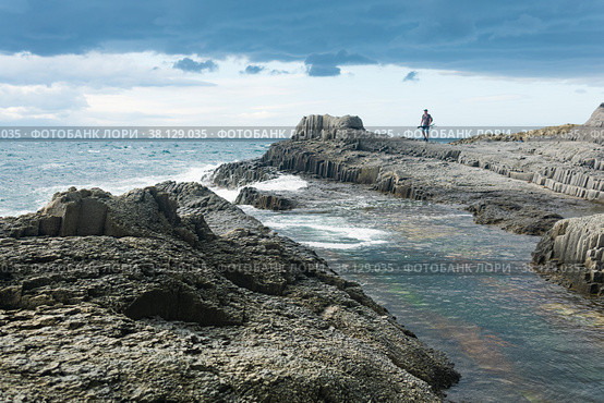 Coastal seascape with beautiful columnar basalt rocks at low tide, fisherman is seen in the distance in blur (2022 год). Редакционное фото, фотограф Евгений Харитонов / Фотобанк Лори