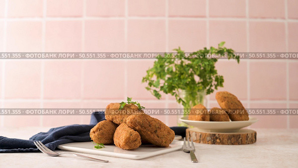 Cod dumplings, or "bolinhos de bacalhau" and parsley leaves on white ceramic dishes in a kitchen counter top. Стоковое фото, агентство Ingram Publishing / Фотобанк Лори