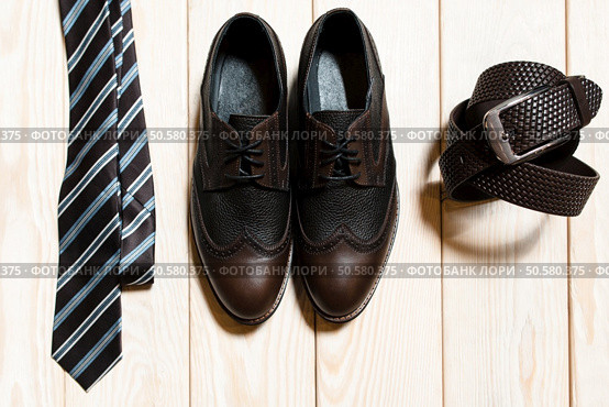 Collection of man’s accessories - new stylish bright footwear, tie and a belt on a dark wooden background. Стоковое фото, агентство Ingram Publishing / Фотобанк Лори