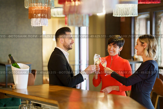 Company of cheerful friendly people in elegant outfits clicking glasses with champagne and proposing toast while celebrating event in restaurant. Group of friends clicking glasses in bar. Стоковое фото, агентство Ingram Publishing / Фотобанк Лори
