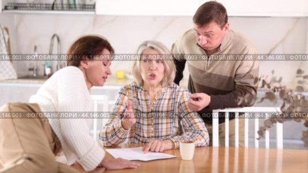 Competitive middle-aged man and woman conflicting and old woman writing inheritance sitting at kitchen table. Стоковое видео, видеограф Яков Филимонов / Фотобанк Лори