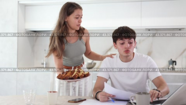 Concentrated guy sitting at computer and a girl persuading to give him pasty in the kitchen. Стоковое видео, видеограф Яков Филимонов / Фотобанк Лори