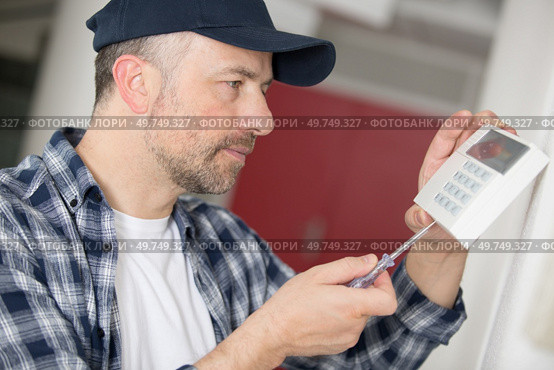 concentrated man screwing a device on the wall. Стоковое фото, агентство Ingram Publishing / Фотобанк Лори