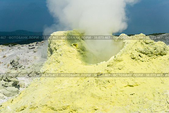 Cone of sulfur deposits around a fumarole in a solfataric field illuminated by the sun against a stormy landscape in the distance. Стоковое фото, фотограф Евгений Харитонов / Фотобанк Лори