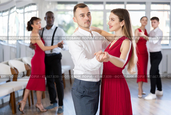 Confident man dancing waltz with female partner in red during group class. Стоковое фото, фотограф Яков Филимонов / Фотобанк Лори