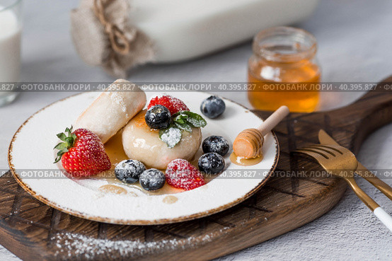 Cottage cheese pancakes, Russian cheesecakes with fresh blueberries, strawberries, honey and mint leaves on a stylish wooden board on a gray concrete table. Natural products. Healthy and delicious breakfast. Стоковое фото, фотограф Photojuli / Фотобанк Лори