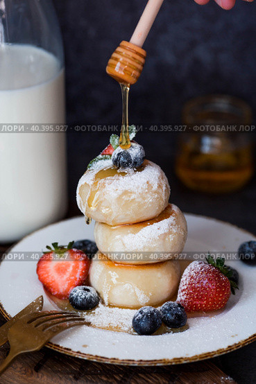 Cottage cheese pancakes, Russian cheesecakes with fresh blueberries, strawberries, honey and mint leaves on a stylish wooden board on a dark background. Natural products. Healthy and delicious breakfast. Стоковое фото, фотограф Photojuli / Фотобанк Лори
