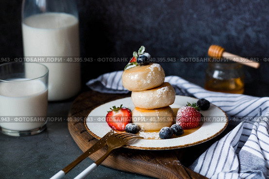 Cottage cheese pancakes, Russian cheesecakes with fresh blueberries, strawberries, honey and mint leaves on a stylish wooden board on a dark background. Natural products. Healthy and delicious breakfast. Стоковое фото, фотограф Photojuli / Фотобанк Лори