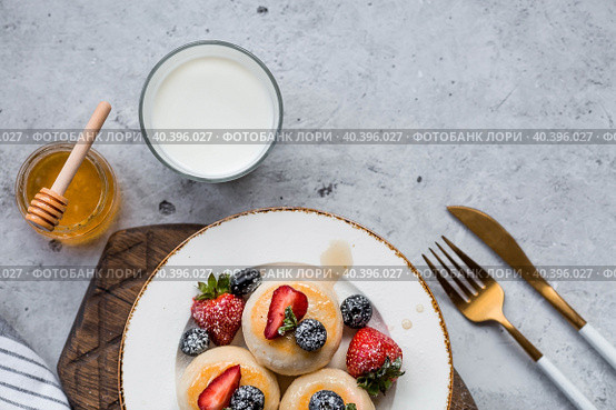 Cottage cheese pancakes, Russian cheesecakes with fresh blueberries, strawberries, honey and mint leaves on a stylish wooden board on a gray concrete table. Natural products. Healthy and delicious breakfast. Стоковое фото, фотограф Photojuli / Фотобанк Лори