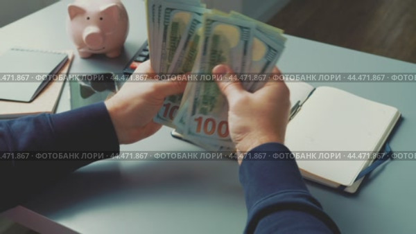 Counting cash at a desk with a piggy bank and notepad in a well-lit room on a weekday afternoon. Стоковое видео, видеограф Сергей Толмачёв / Фотобанк Лори