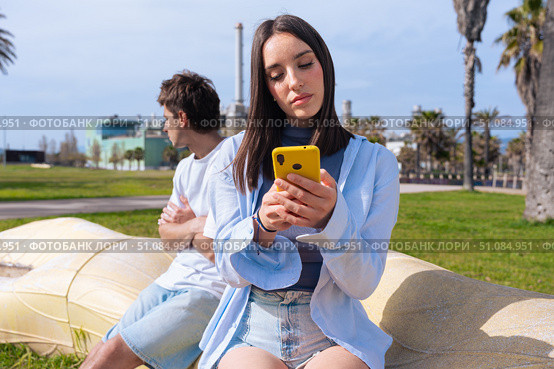 Couple conflict outdoors, woman on phone, man upset. Стоковое фото, фотограф Raquel Corcoles Mendez / Фотобанк Лори