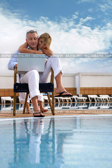 Couple looking at a laptop by a pool. Стоковое фото, агентство Ingram Publishing / Фотобанк Лори