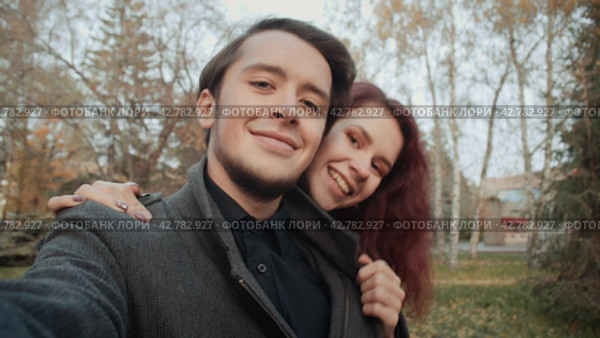 Couple of loving young people is taking photo themselves in the city autumnal park. Стоковое видео, видеограф EStarodubov / Фотобанк Лори