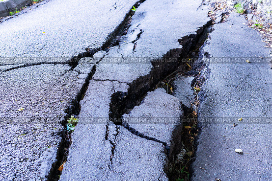 Cracked asphalt road surface damaged by landslide, showcasing deep fissures and uneven terrain, illustrating the impact of natural disasters on infrastructure and environment. Стоковое фото, фотограф Елена Гоосен / Фотобанк Лори