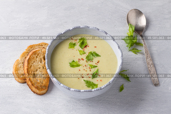 Cream soup of stalked celery with cream, garnished with celery leaves, pink pepper and served with crispy toast on a light gray background, top view. Стоковое фото, фотограф Ольга Лепёшкина / Фотобанк Лори