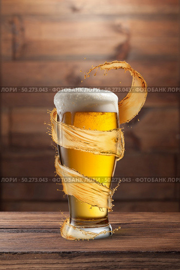Creative flying spiral yellow splash aroung full glass of fresh cold light beer on a wooden table against wall from wood, copy space.. Glass of light fresh beer with flying spiral splash around mug. Стоковое фото, агентство Ingram Publishing / Фотобанк Лори