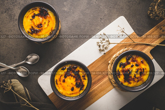 Creme brulee. Bowls with French vanilla cream dessert with caramelised sugar on top, spoons, dark rustic table. Стоковое фото, агентство Ingram Publishing / Фотобанк Лори