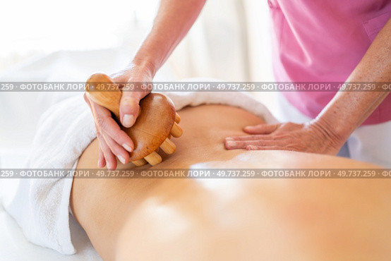 Crop anonymous therapist massaging with wooden therapy tool on back of anonymous client during physiotherapy session in osteopathy clinic. Crop masseur massaging back of client in physiotherapy clinic with wooden therapy tool. Стоковое фото, агентство Ingram Publishing / Фотобанк Лори