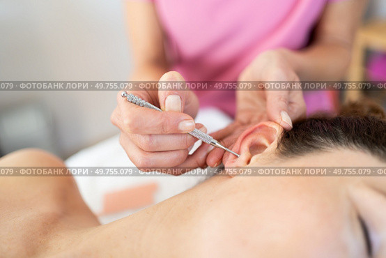 Crop professional chiropractor woman applying facial stimulation massage ear pen on female client during auriculotherapy beauty procedure in modern salon. Auriculotherapy treatment on female ear with flexible massage brass ear pen. Стоковое фото, агентство Ingram Publishing / Фотобанк Лори