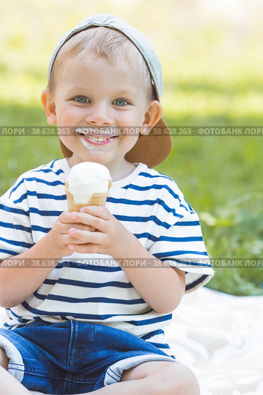 Cute, happy little boy with a beautiful smile and dirty face eating ice cream outdoors on a hot summer day. A child enjoys a sweet dessert during the summer holidays. Стоковое фото, фотограф Photojuli / Фотобанк Лори