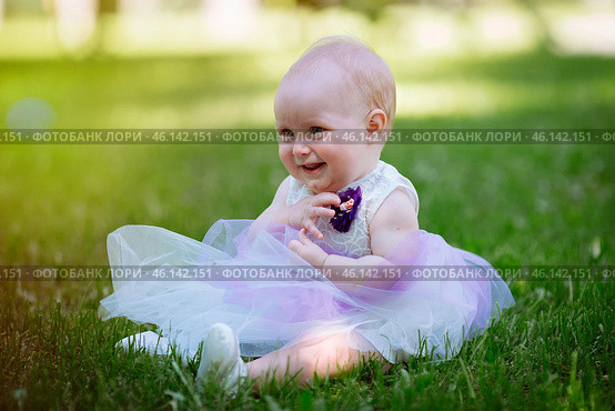 Cute little baby girl sitting on the grass in the Park on a warm summer day. Walking and playing in the fresh air. Стоковое фото, фотограф Иван Карпов / Фотобанк Лори